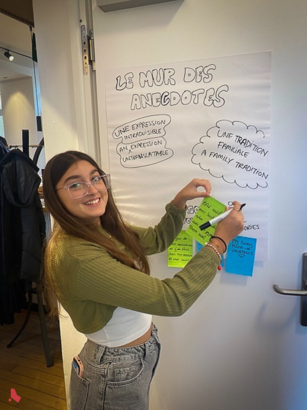 Une jeune participante colle un post-it sur le « Mur des anecdotes » à l'Afterwork interculturel