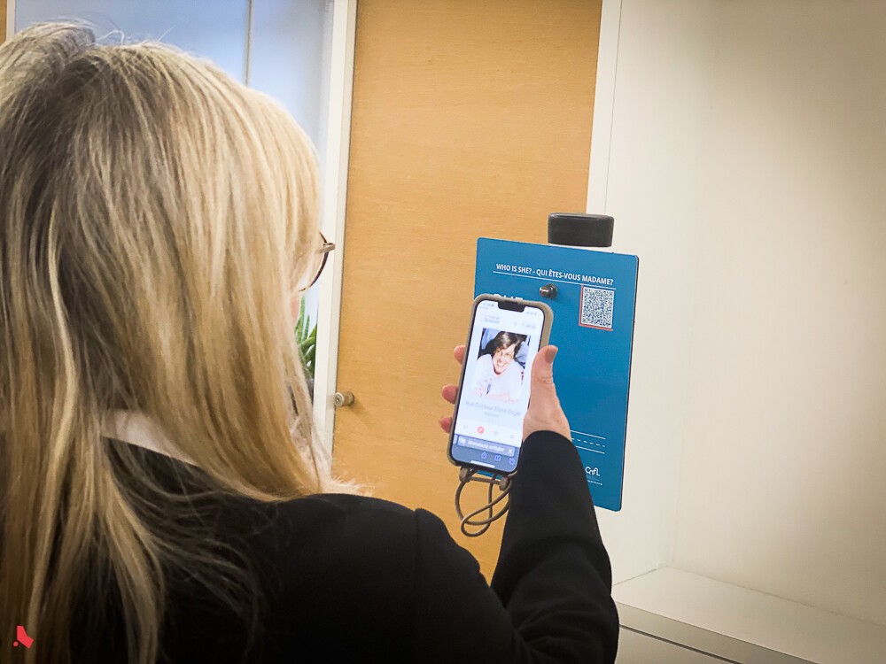 Une femme scanne le code QR du panneau « Rues au féminin » et découvre sur son téléphone le portrait de la Dr Elvire Engel
