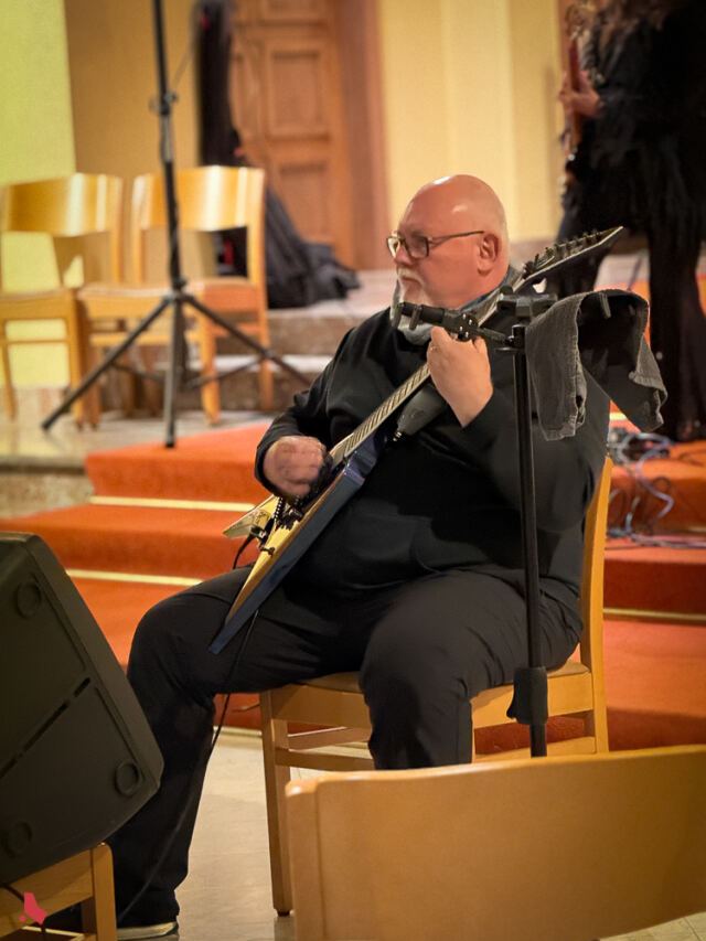 Un guitariste assis joue de la guitare électrique lors du concert « Metal & Pipes »