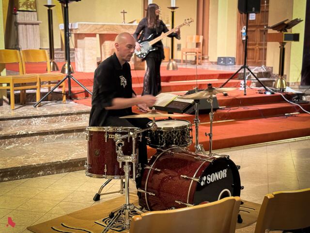 Le batteur du groupe ShadoWhisperS joue au pied du chœur, devant la bassiste, lors du concert « Metal & Pipes »