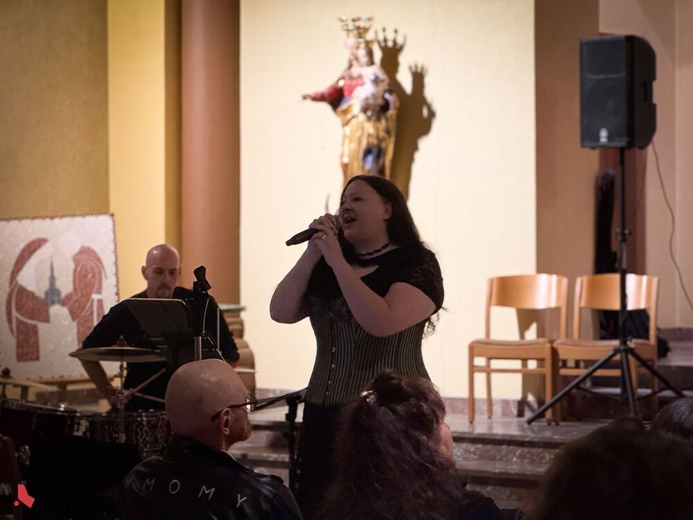 La chanteuse du groupe ShadoWhisperS chante au micro devant le public, avec le batteur derrière elle, lors du concert « Metal & Pipes »
