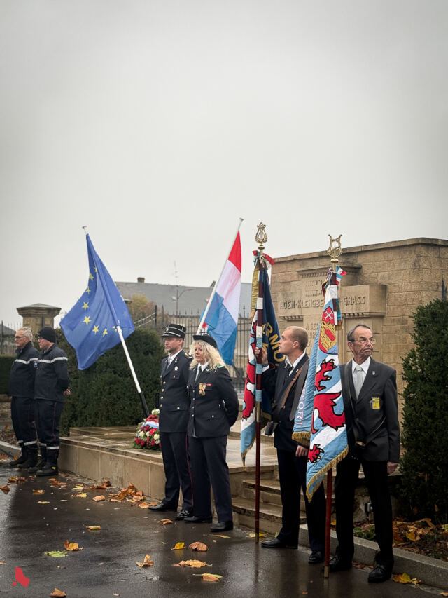 Des porte-drapeaux et des sapeurs-pompiers devant le monument aux morts du cimetière Hagen-Kleinbettingen