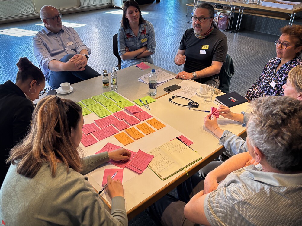 Des participant·e·s discutent autour d'une table couverte de fiches colorées lors de l'atelier citoyen sur le bénévolat en avril 2025 au centre culturel Al Schmelz