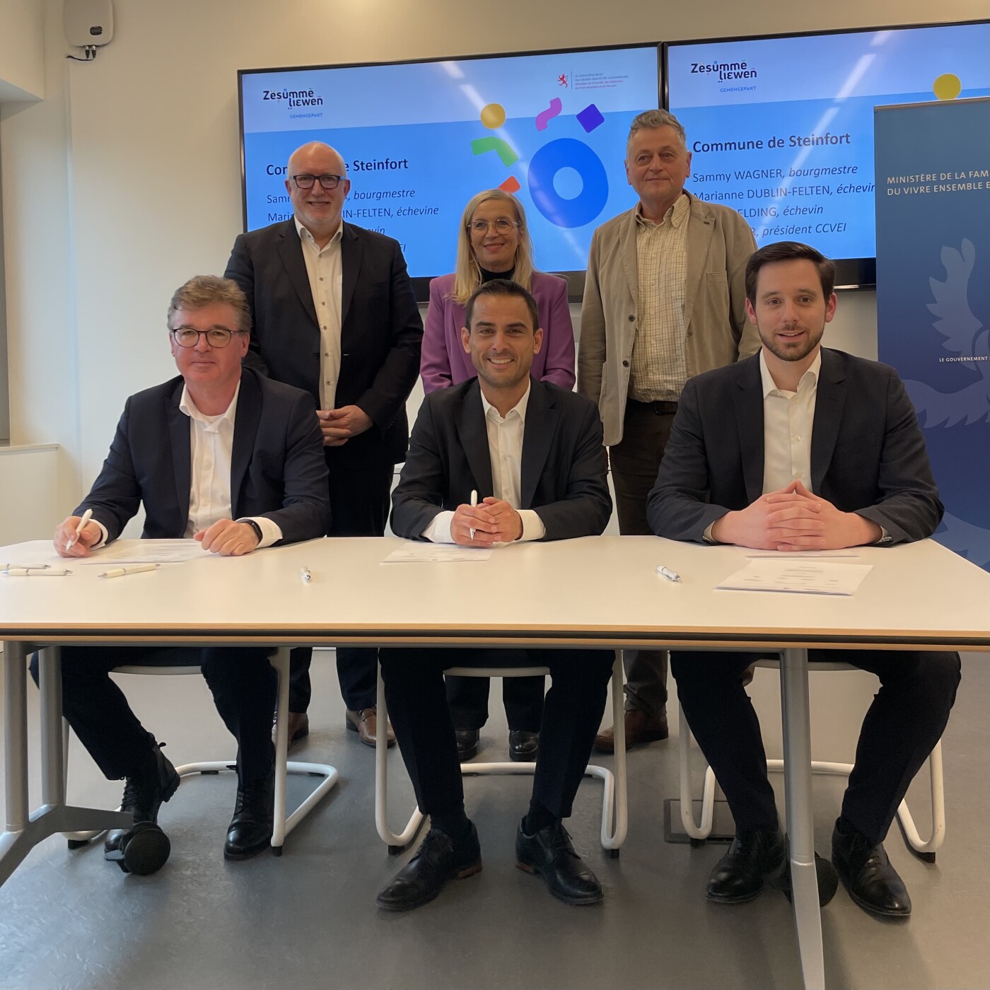 Signature du Gemengepakt « Zesumme liewen » le 27 mars 2027 : six personnes (dont Max Hahn, Sammy Wagner, Guy Erpelding, Marianne Dublin-Felten et Alain Faber) réunies autour d'une table, devant les logos du ministère