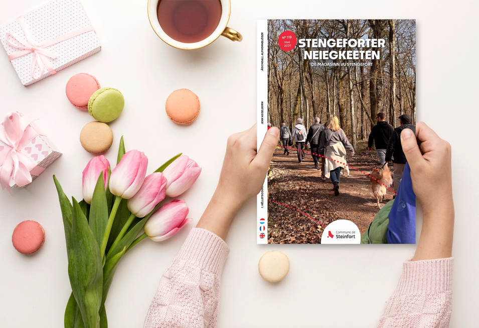 Couverture du magazine communal Stengeforter Neiegkeeten n°119 (mai 2026), posée sur une table avec tulipes roses et macarons. La photo de couverture montre un groupe de personnes et un chien marchant sur un sentier forestier balisé.