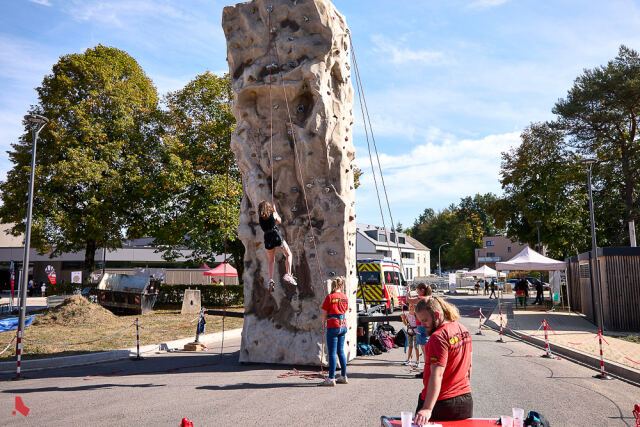 Une jeune grimpeuse encordée escalade une tour mobile en forme de rocher, assurée par une animatrice