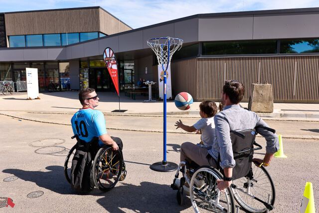 Un enfant assis sur les genoux d'un homme en fauteuil roulant lance un ballon vers un panier de basket