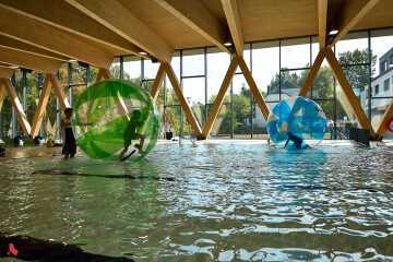 Deux enfants marchent sur l'eau de la piscine communale, à l'intérieur de grandes bulles gonflables transparentes