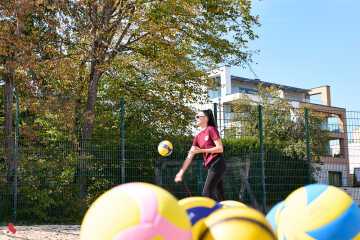 Une joueuse frappe un ballon sur un terrain de beach-volley, avec des ballons colorés au premier plan
