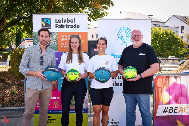 Sammy Wagner et Guy Erpelding posent avec les deux représentantes du comité d'école avec des ballons labellisés Fairtrade devant les panneaux de Fairtrade Lëtzebuerg