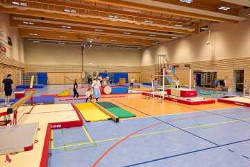 Hall sportif aménagé en parcours de gymnastique, avec des enfants accompagnés sur les agrès