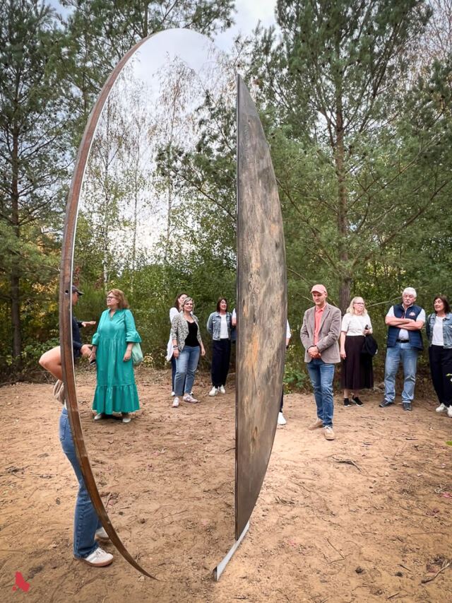 Les invité·e·s entourent la sculpture « Transformation », dont le miroir reflète les arbres, lors de son inauguration